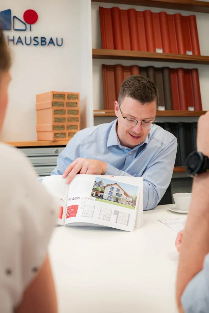 Berater blättert mit Kunden im Hauskatalog, Nahaufnahme