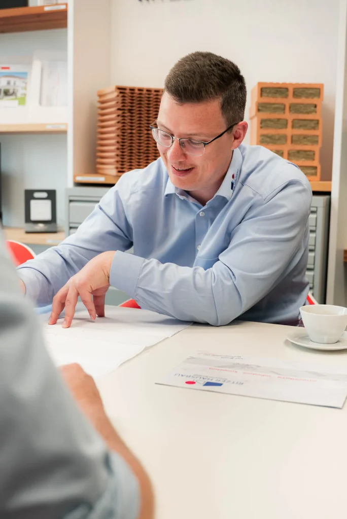 Berater erklärt Bauplan am Schreibtisch mit Firmenbroschüre
